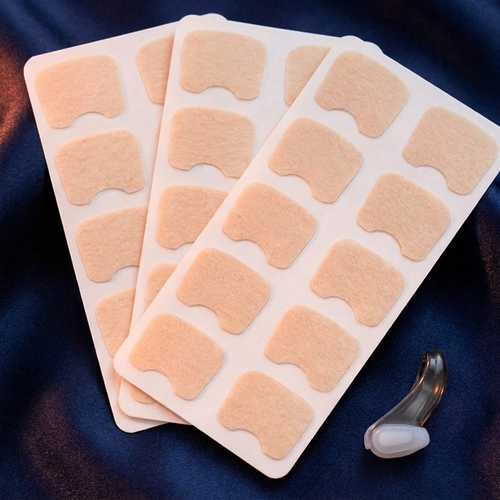 Trois planches de bandelettes nasales Nuit Nette et le clip nasal réutilisable offert, en plastique fumé gris translucide, posés sur satin bleu nuit.